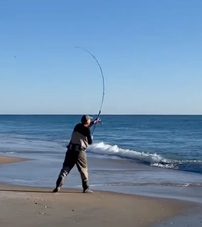 Photo of a man with a rod casting out a surf fishing rig at the beach